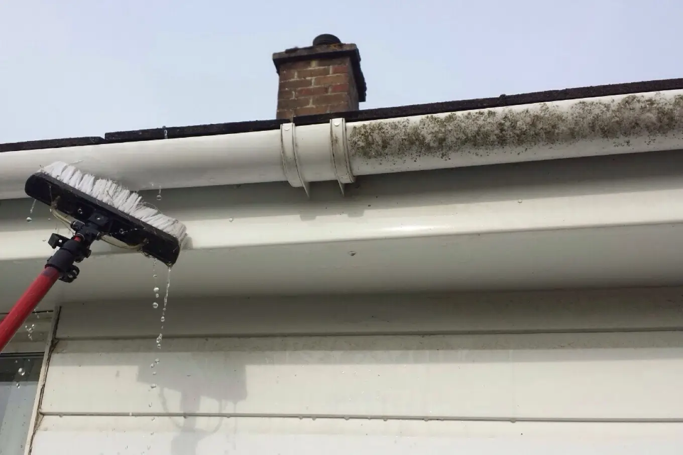 Water-fed brush cleaning white guttering, fascia and soffits