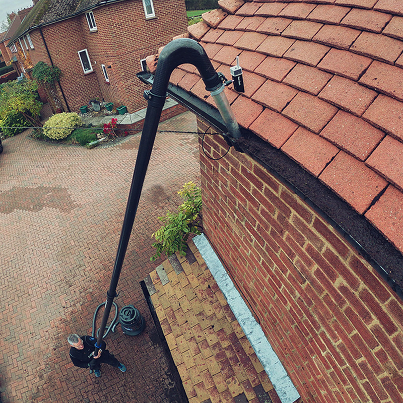 Gutter vacuum clearing debris from a tiled-roof home