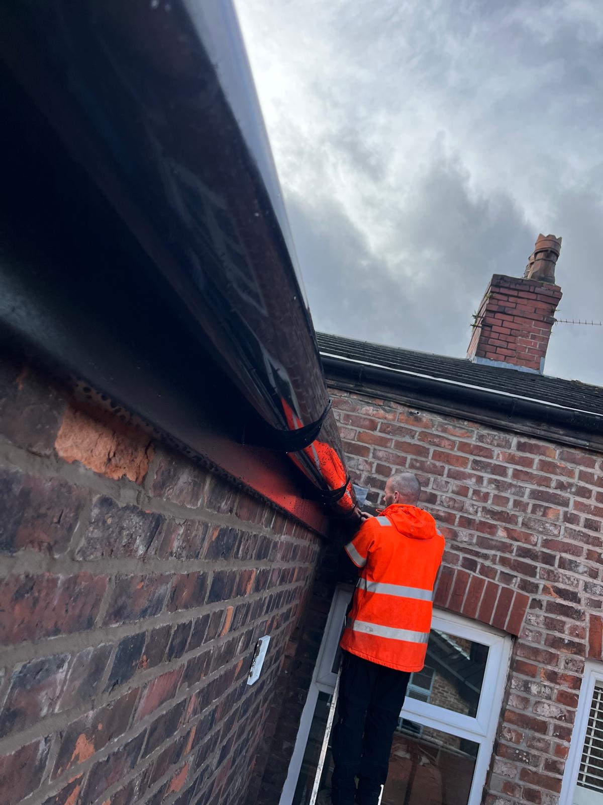 Worker on a ladder repairing guttering on a brick home